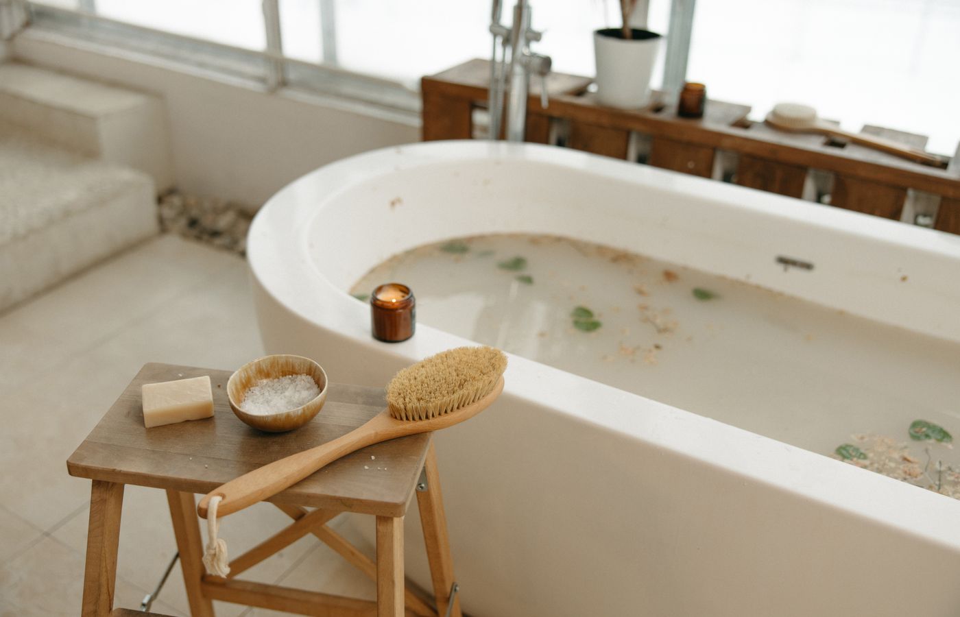 Relaxing spa bath setup with luxurious essentials including soap, brush, salts, and candle.