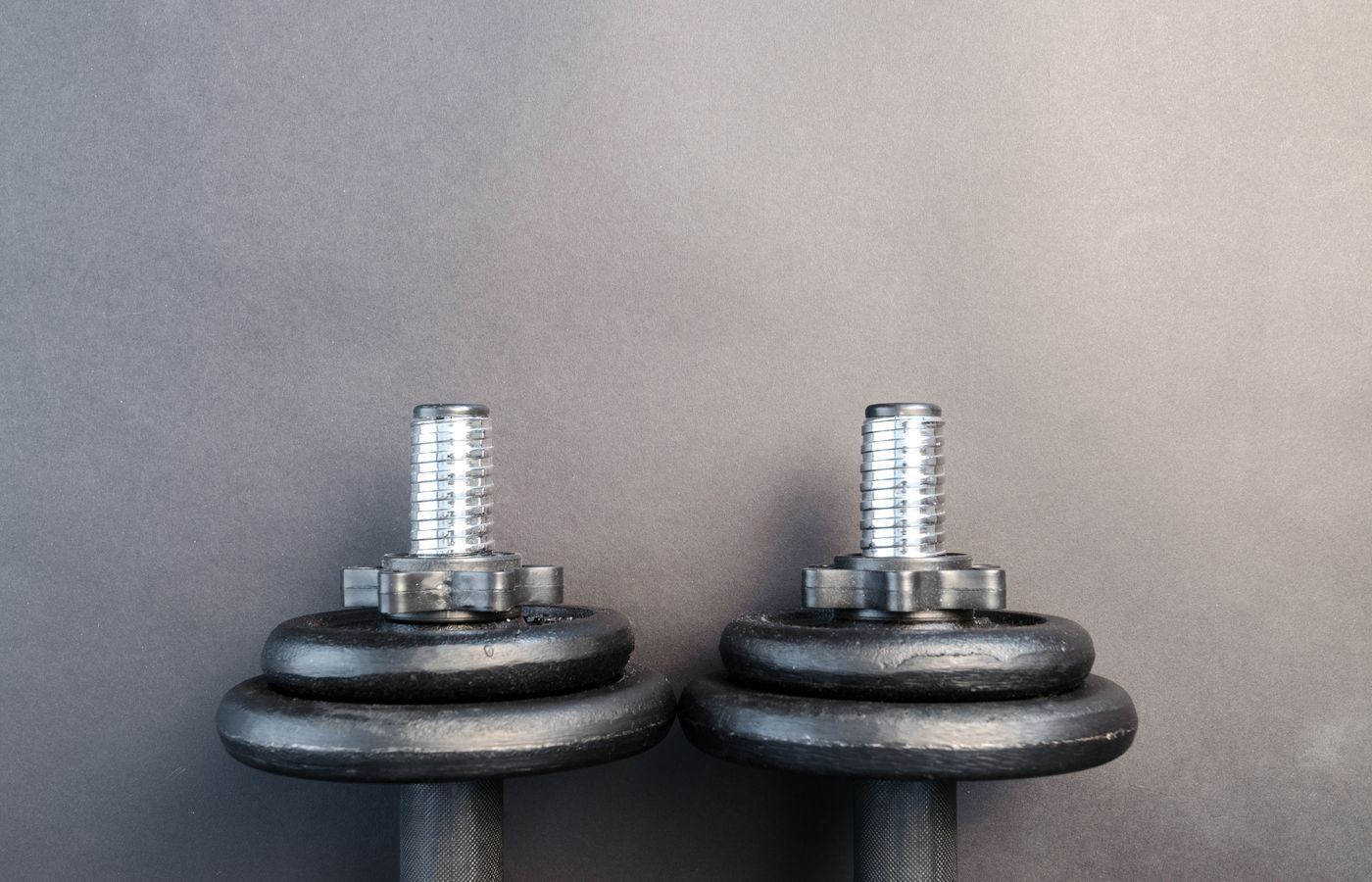 Close-up of two iron dumbbells on a gray background, perfect for strength training images.