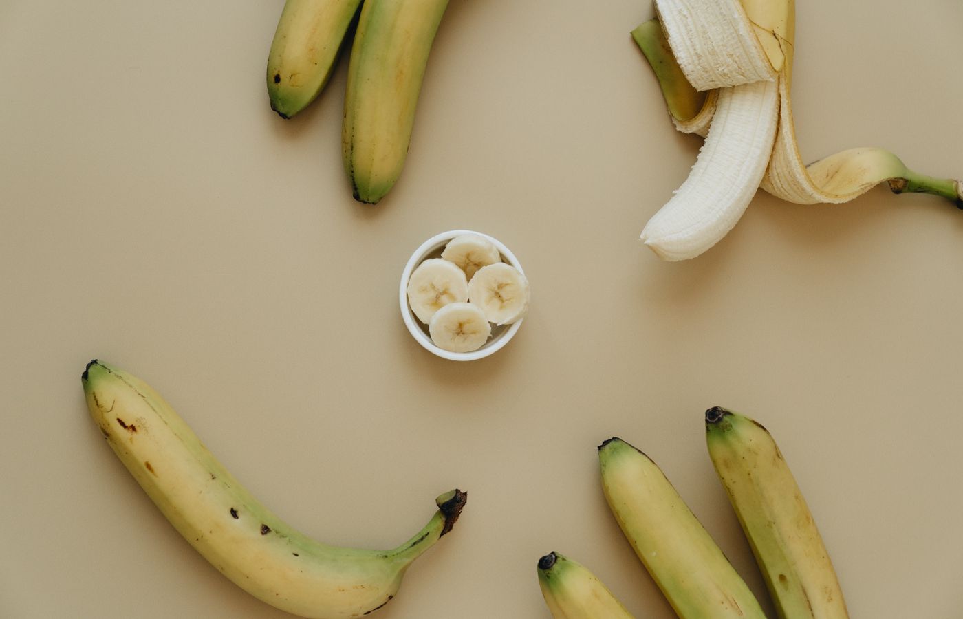 Top view of whole and sliced bananas artfully arranged on a neutral background.