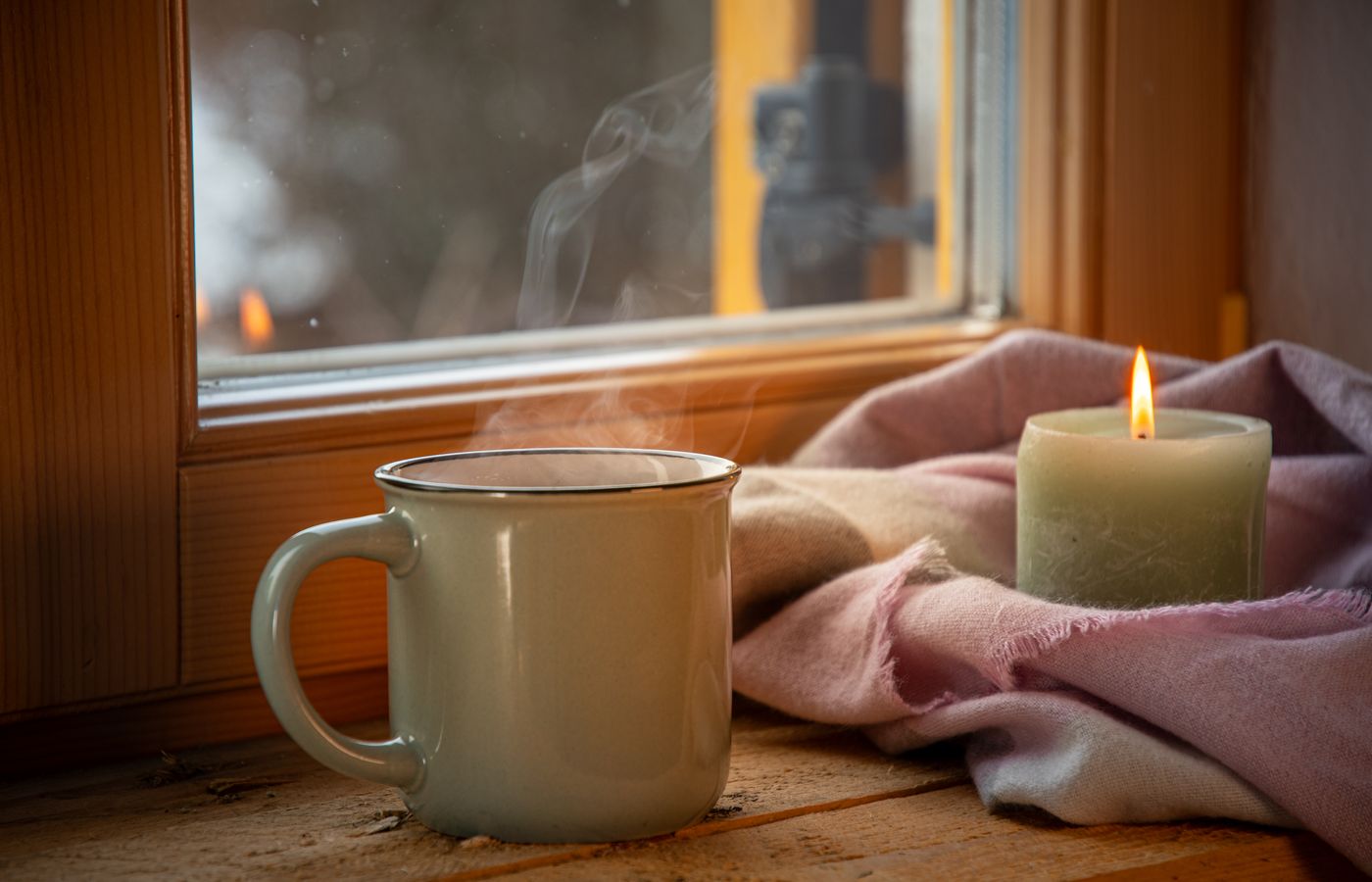 A warm cup of coffee and a candle create a cozy ambiance by the window.