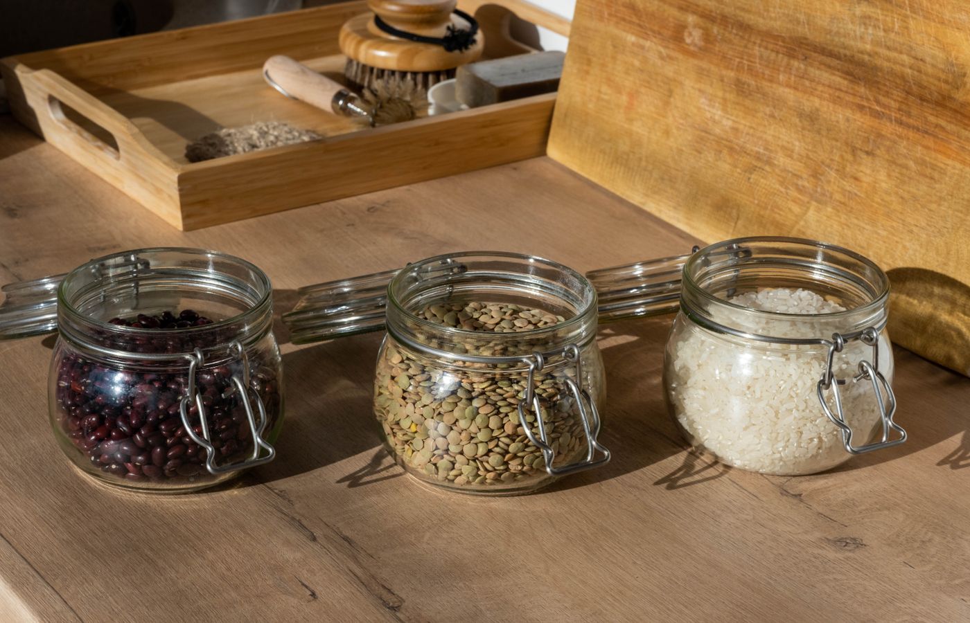 Glass jars of beans, lentils, and uncooked rice on a wooden table with warm lighting.