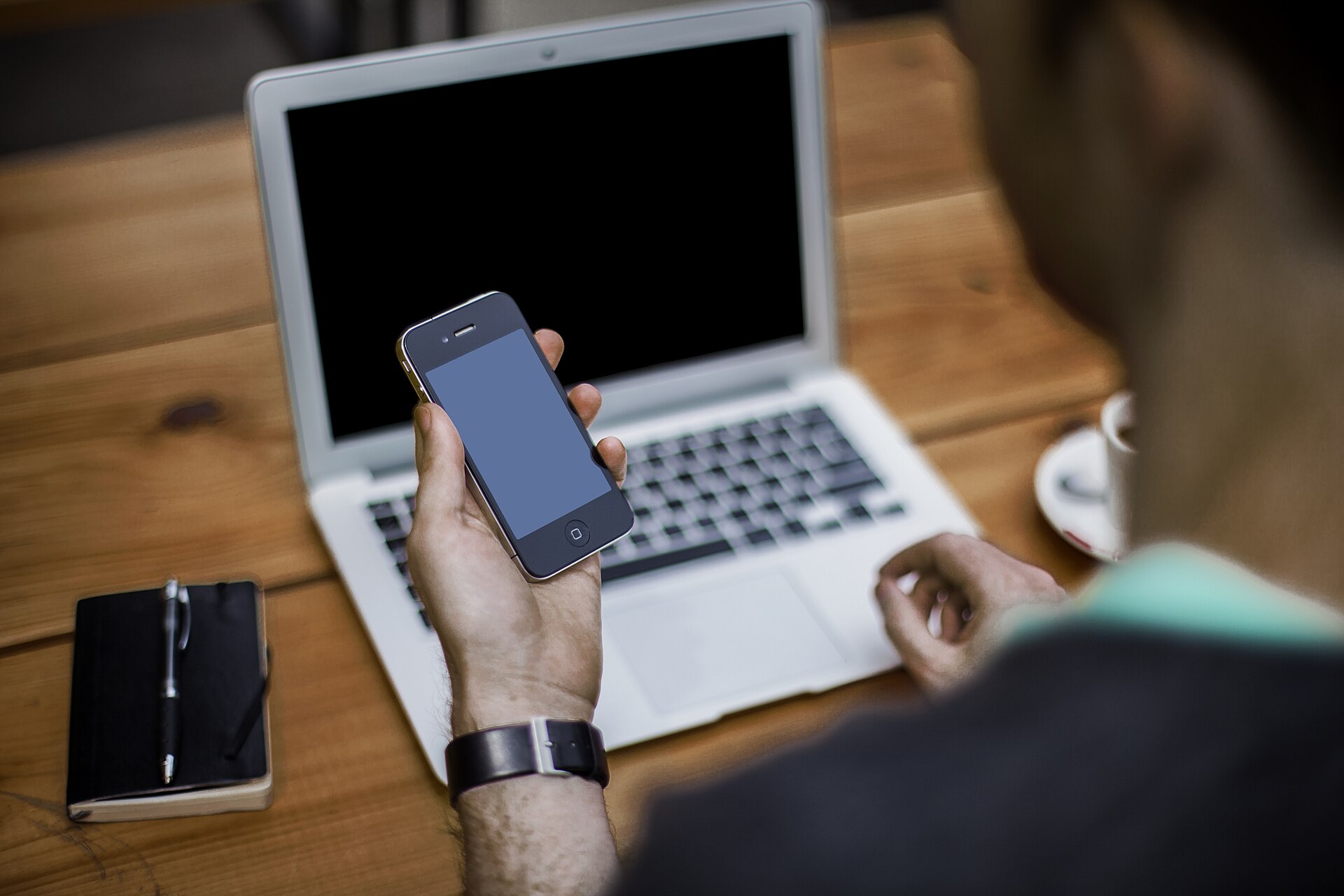 Man using a smartphone beside an open laptop